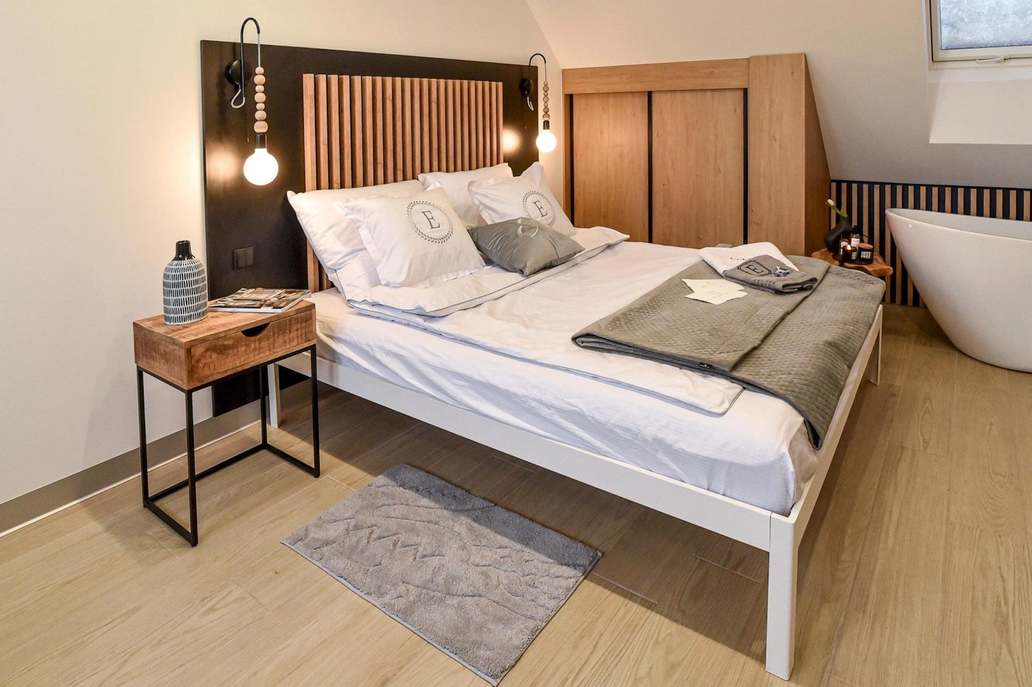 Ein modernes Schlafzimmer mit einem Bett, Nachttischen, einer Stehlampe, einer Nachttischlampe, einem Teppich und einer Badewanne.