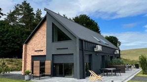 Una casa moderna con techo inclinado, ventanas amplias y un patio con mobiliario exterior.