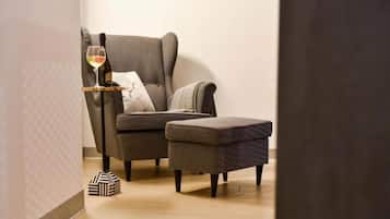 Un salon moderne avec un fauteuil gris, un petit pouf, un verre de vin et une boîte décorative noir et blanc posée sur le sol.