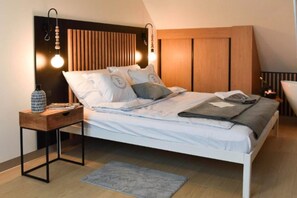 A modern bedroom with a bed, bedside table, lamp, and a decorative wall panel.