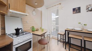 A modern kitchen with a stove, oven, and wooden cabinets. There is a dining table with chairs and a view of the outdoors through a window. - Spacious Apartment with Balcony | Parking | Close to Attractions (Warszawa)