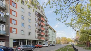 A multi-story residential building with balconies, a parking area with cars, and a clear sky. - Spacious Apartment with Balcony | Parking | Close to Attractions (Warszawa)