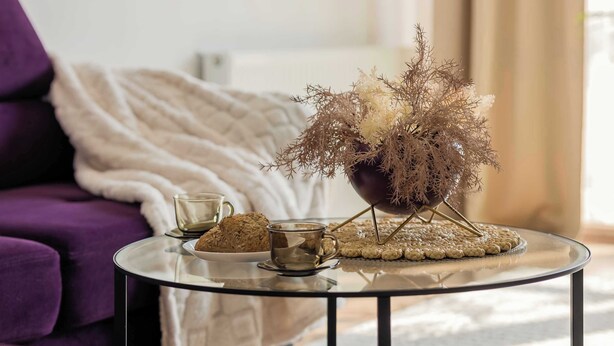 A purple sofa, a glass coffee table with a decorative plant, a cup, and a cookie. - Spacious Apartment with Balcony | Parking | Close to Attractions (Warszawa)
