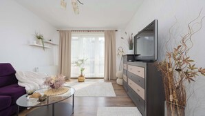 A modern living room with a sofa, coffee table, TV, and decorative plants. - Spacious Apartment with Balcony | Parking | Close to Attractions (Warszawa)