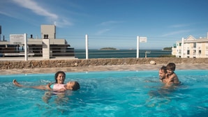 A swimming pool with clear blue water, surrounded by a stone wall and buildings in the background. - Mirante dos Ingleses (Florianopolis)