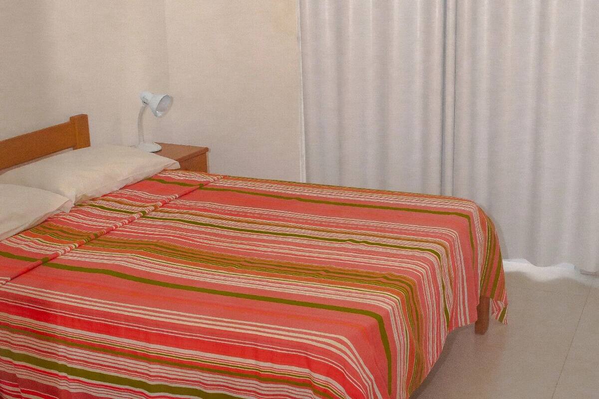 Una habitación con dos camas, una mesita de noche con lámpara y una ventana con cortinas.