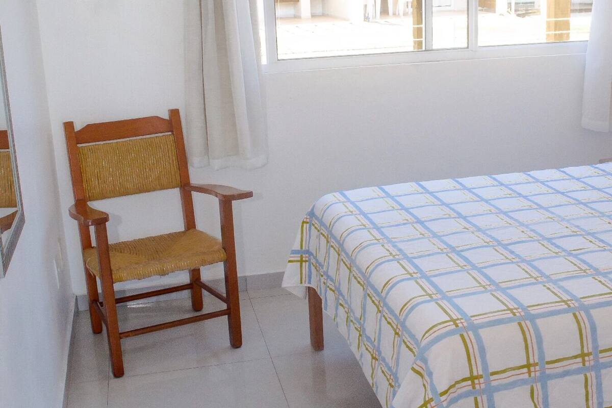 Una habitación con una cama, una silla, un ventanal y una puerta.