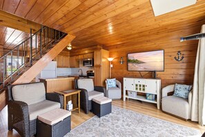 Un interior de madera con una escalera, muebles de mimbre, una cocina y un televisor.