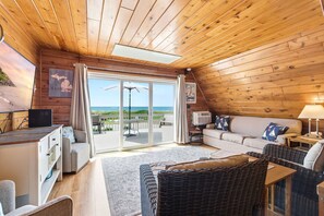 Una cabaña acogedora con interior de madera, un sofá, una mesa de comedor y vista a la playa.