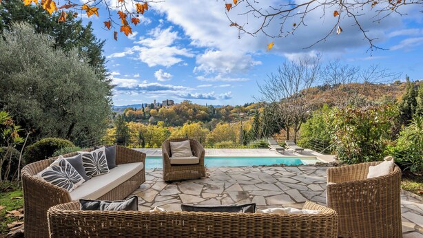 Un patio con mobili in vimini, una piscina e vista su una collina alberata.