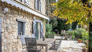 Un edificio in pietra con un patio che presenta un tavolo e sedie di legno, circondato da piante in vaso e alberi.