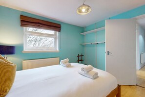 Ein Schlafzimmer mit Bett, Fenster mit Jalousien, Heizkörper, Kleiderschrank und Tür.