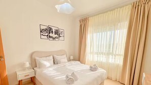 Habitación de hotel con una cama grande, una mesita de noche, un escritorio y una ventana con cortinas.