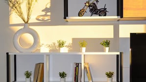 Una sala de estar moderna con un banco de madera, un estante fijado a la pared con plantas y libros, y una fotografía de una motocicleta.