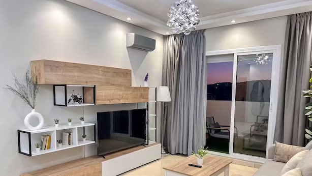 Una sala de estar moderna con sofá, una mesita de centro, televisor y un balcón con vistas.