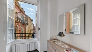 Ein Zimmer mit großem Fenster, Heizkörper, einem Holzschrank, einer Lampe und einem Spiegel.