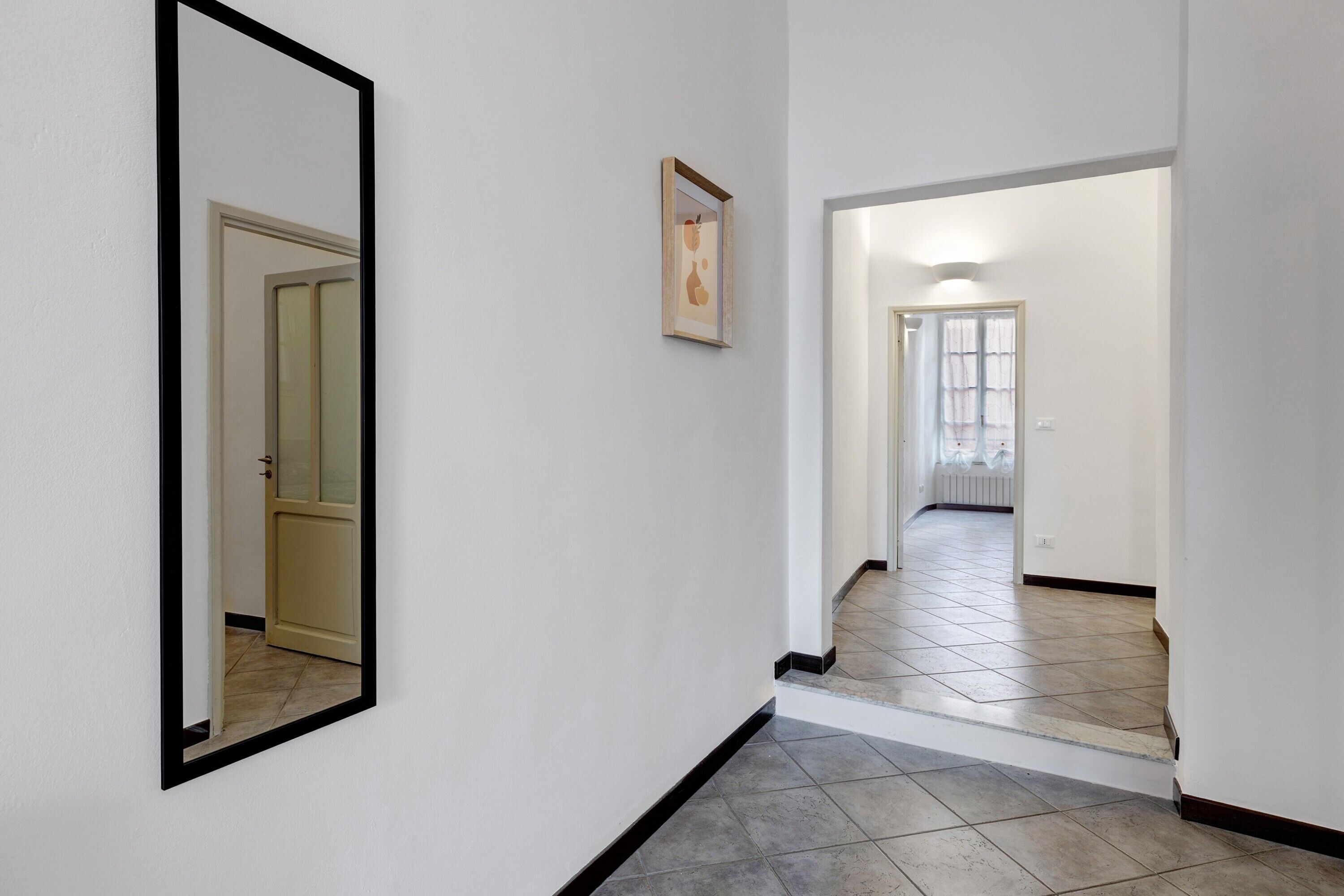 A hallway with a mirror, a framed picture, and a door leading to another room.