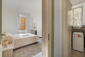 Une chambre à coucher avec un lit, une table de chevet, une lampe, une fenêtre et un lave-linge.