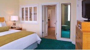 A hotel room with a bed, a nightstand, a lamp, a television, a wardrobe, and a door leading to another room. - Harborside Resort at Atlantis-2 Bedrooms and Full Resort Access (N.P)