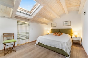 A bedroom with a skylight, a bed with a green headboard, a wooden chair, and a nightstand with a lamp. - Apartment 'Casa Di Gaia' with Wi-Fi and Air Conditioning (Carloforte)