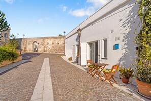 A cobblestone street leading to a building with a white facade, a door, and a small table with chairs. - Apartment 'Casa Di Gaia' with Wi-Fi and Air Conditioning (Carloforte)