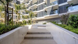 Ein modernes Gebäude mit Betonstufen, die zu einem Balkon führen, umgeben von Grünflächen.