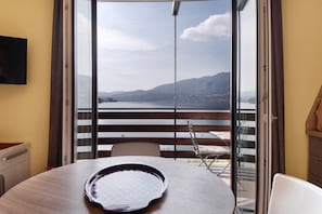 Ein Zimmer mit Tisch, Stühlen, Fernseher und Blick auf einen See und Berge durch eine Schiebetür.