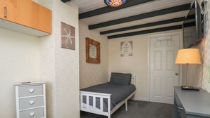 Ein Schlafzimmer mit Bett, Schminktisch, Nachttisch, Kommode mit herzförmigen Schubladen, einem Kunstwerk mit Seestern und einer Lampe. Auf der Wand befindet sich ein Schild.