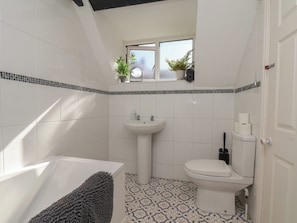 A bathroom with a bathtub, toilet, sink, and a window with plants. - Marina House (Whitby)