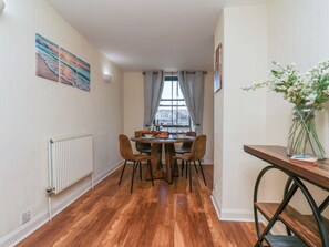 A dining area with a table, chairs, a vase of flowers, and a window with curtains. - Marina House (Whitby)