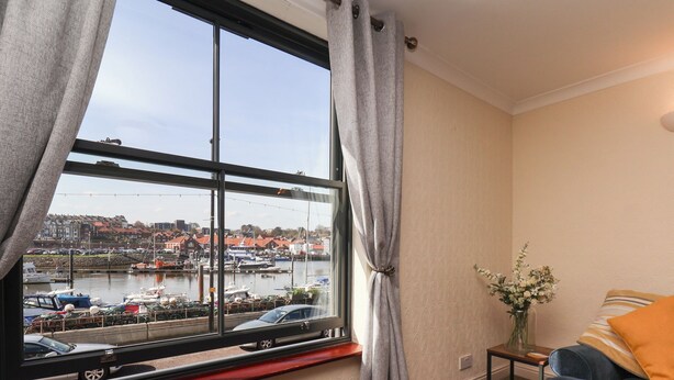 Ein Zimmer mit großem Fenster mit Blick auf eine Marina, einem Sofa, einem kleinen Tisch und einer Vase mit Blumen.