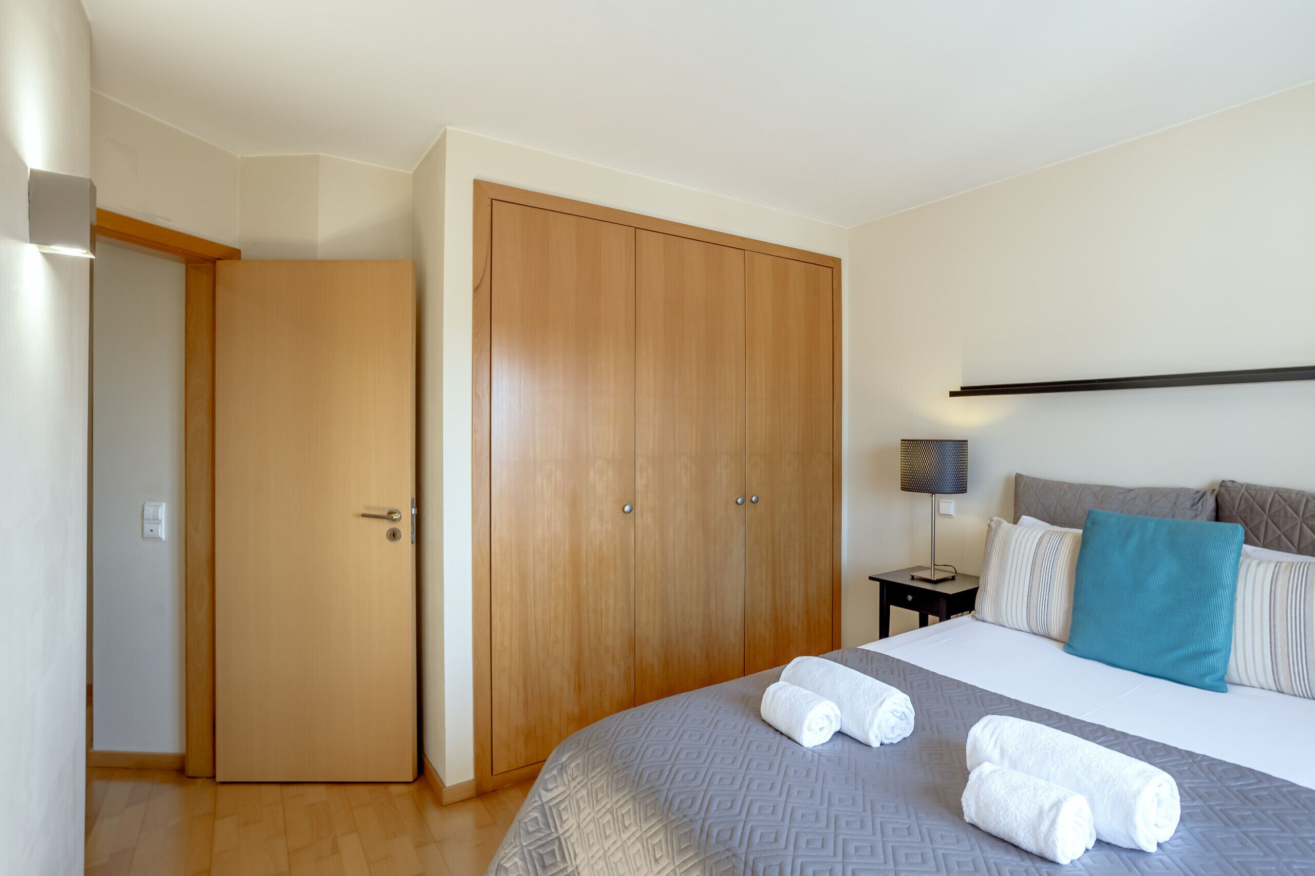 Een slaapkamer met een bed, een kledingkast, een nachtkastje en een lamp.