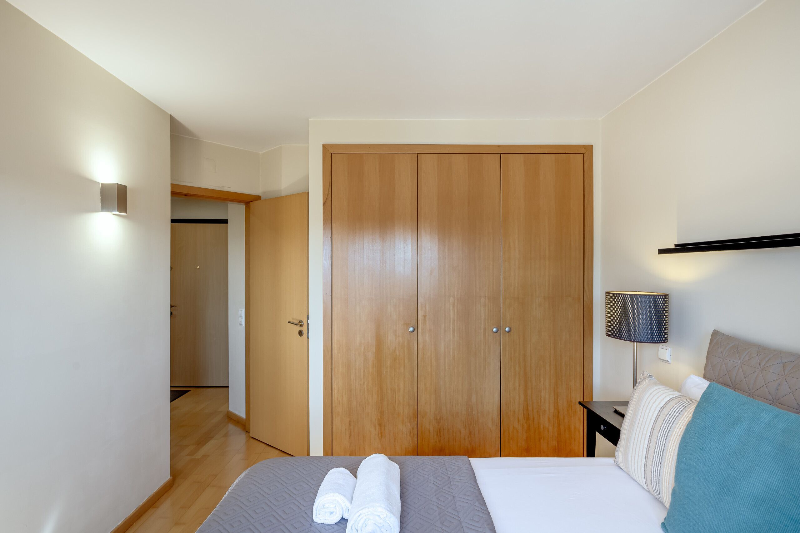 Ein Schlafzimmer mit Bett, Schrank, Nachttisch mit Lampe und Wandleuchte.