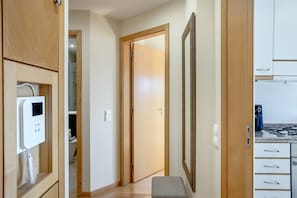 Un pasillo con armarios de madera, un banco, una puerta que da a un baño y una zona de cocina con estufa.
