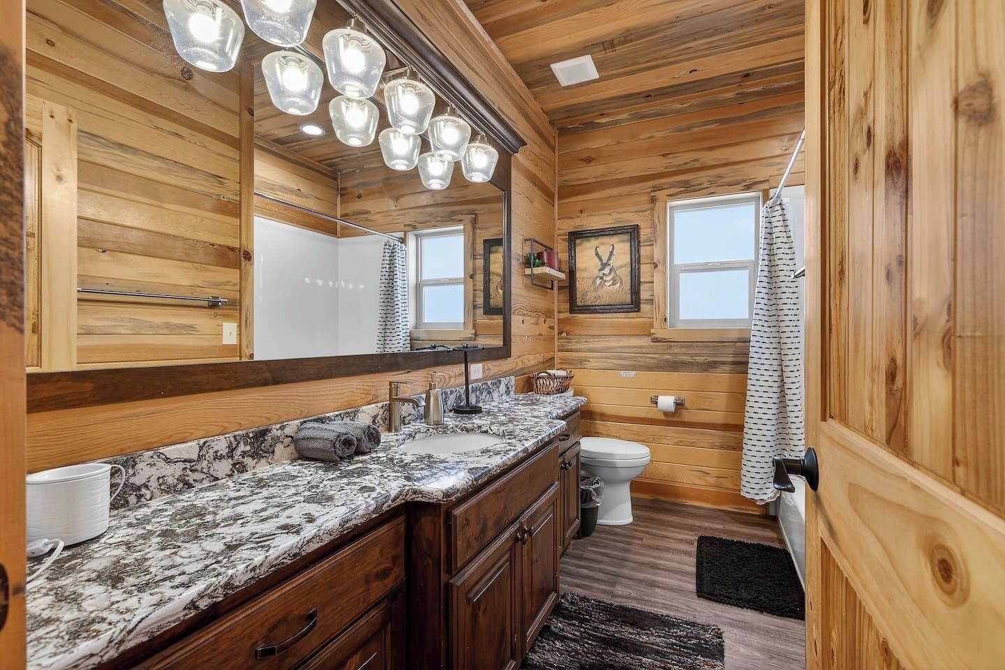 Un bagno in una cabina di legno con un piano di marmo, un lavandino, un water e una tenda per la doccia.