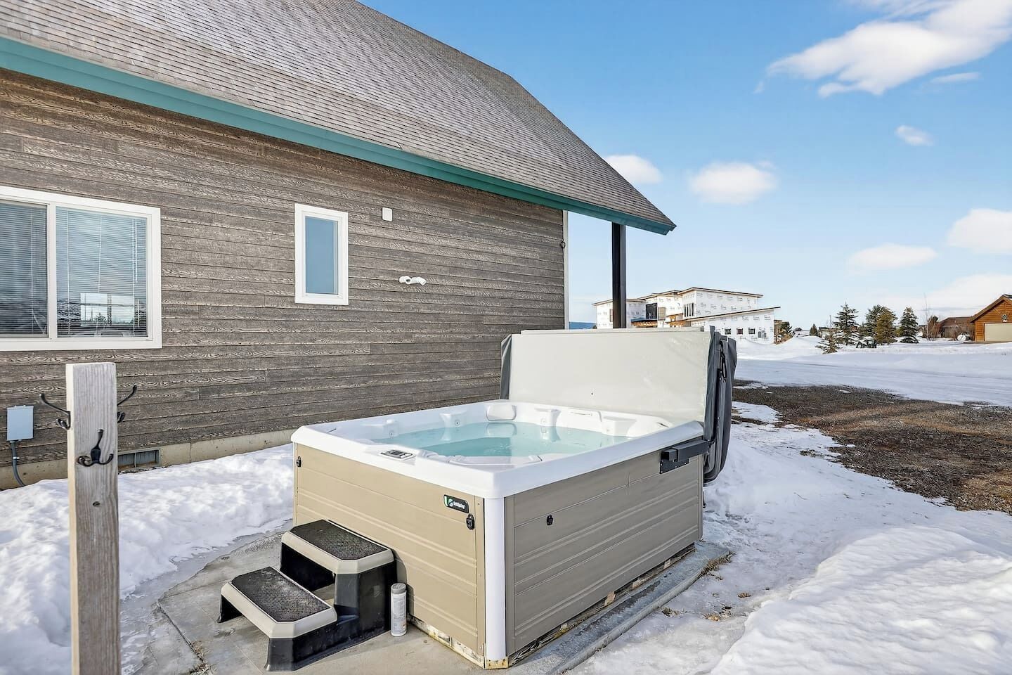 A hot tub outside a building with a wooden exterior, a window, and a clear sky.