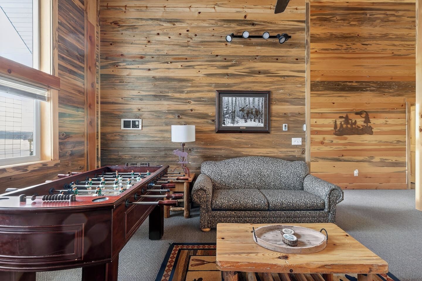 A cozy room with a wooden wall, a foosball table, a patterned sofa, and a small table with a decorative item.
