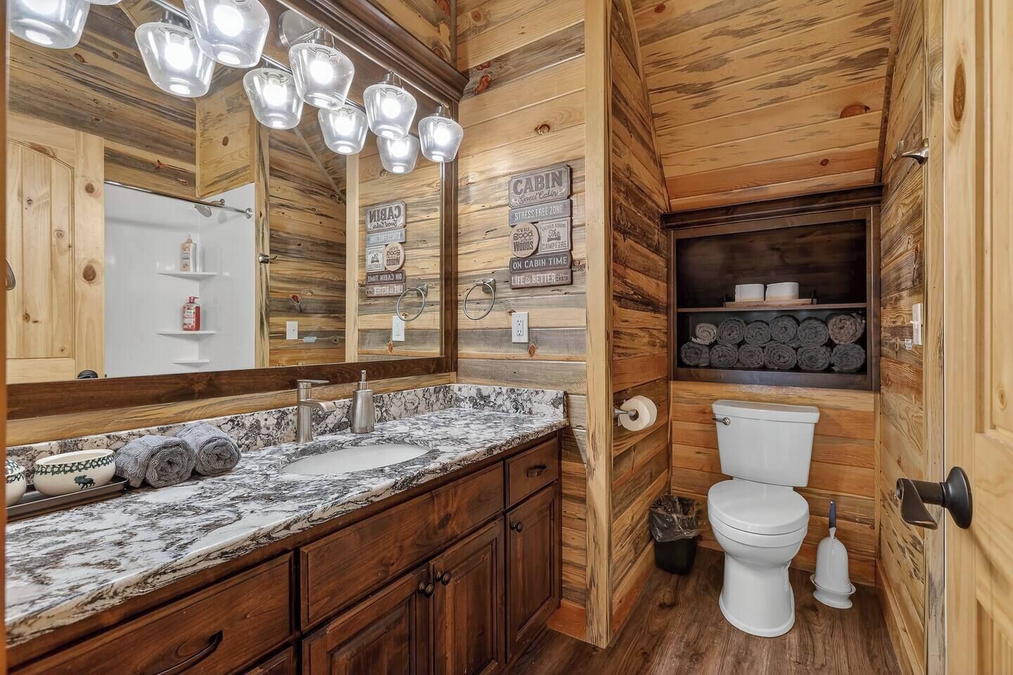 Une salle de bain de style rustique, avec un lavabo en marbre, des meubles en bois, des toilettes et un miroir avec éclairage intégré.