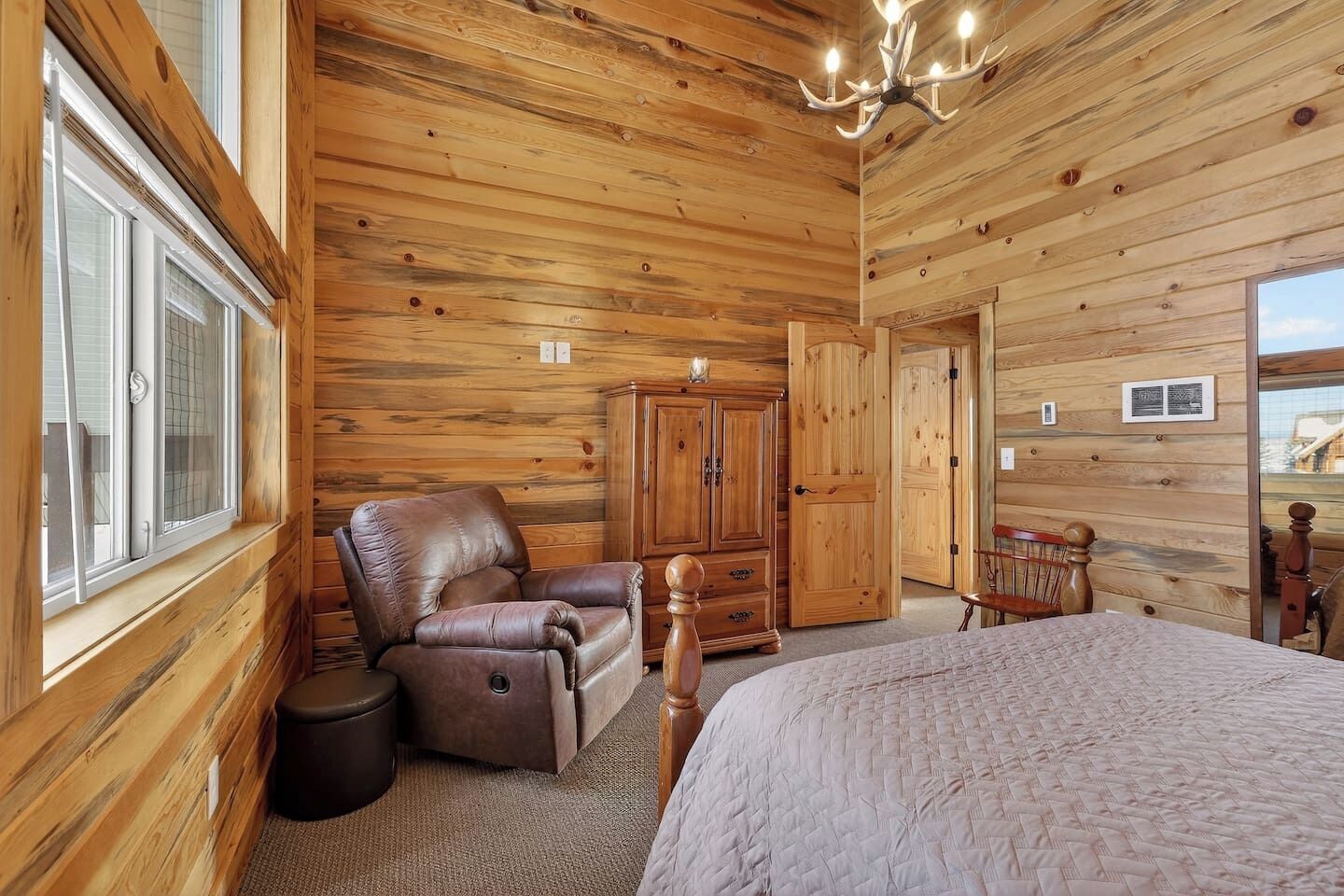 A wooden-paneled room with a bed, a leather chair, a wooden wardrobe, and a door leading to another room.