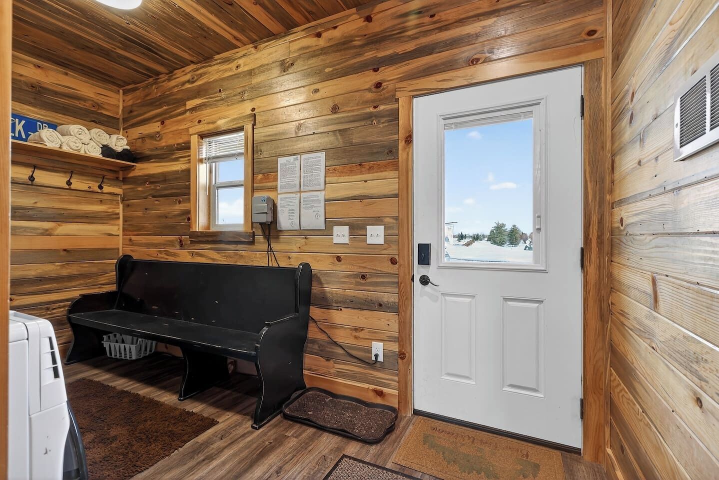 A wooden interior with a bench, a door, and a window with a view.