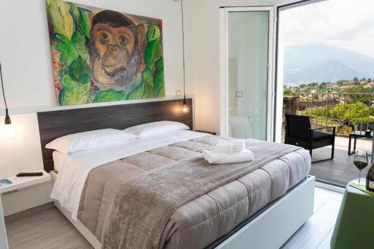 A bedroom with a bed, a painting, a balcony with a view, and a chair.