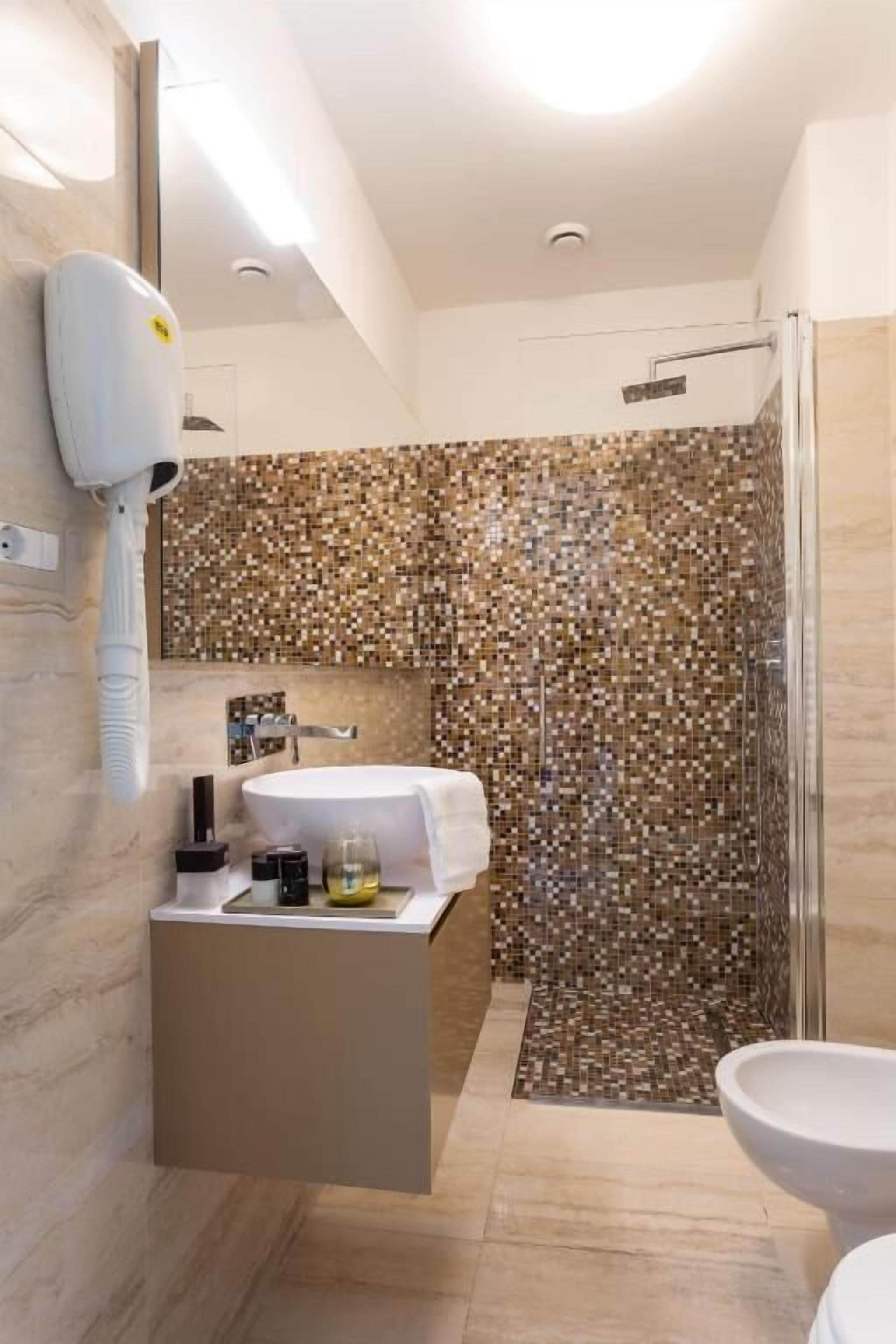 A modern bathroom with a shower, a sink, and a hairdryer mounted on the wall.