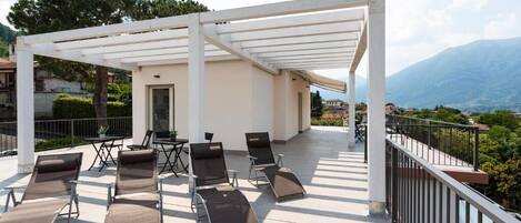 Un espacio de descanso techado al aire libre con sillones reclinables y una mesa, con vistas a un paisaje montañoso.