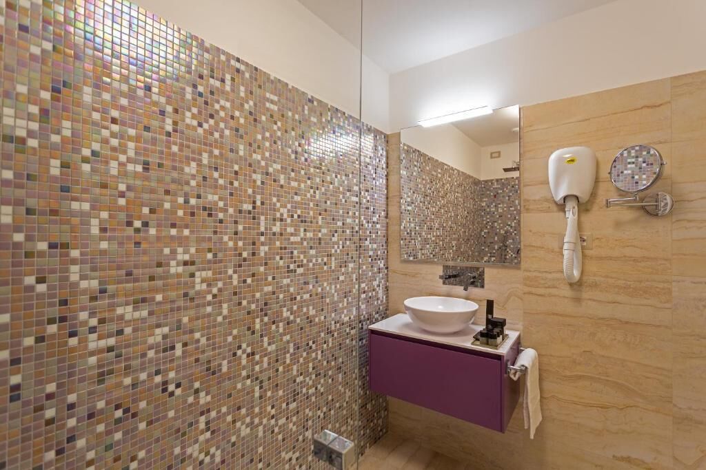 Une salle de bain avec des murs recouverts de mosaïques, un lavabo, un miroir et un sèche-cheveux.