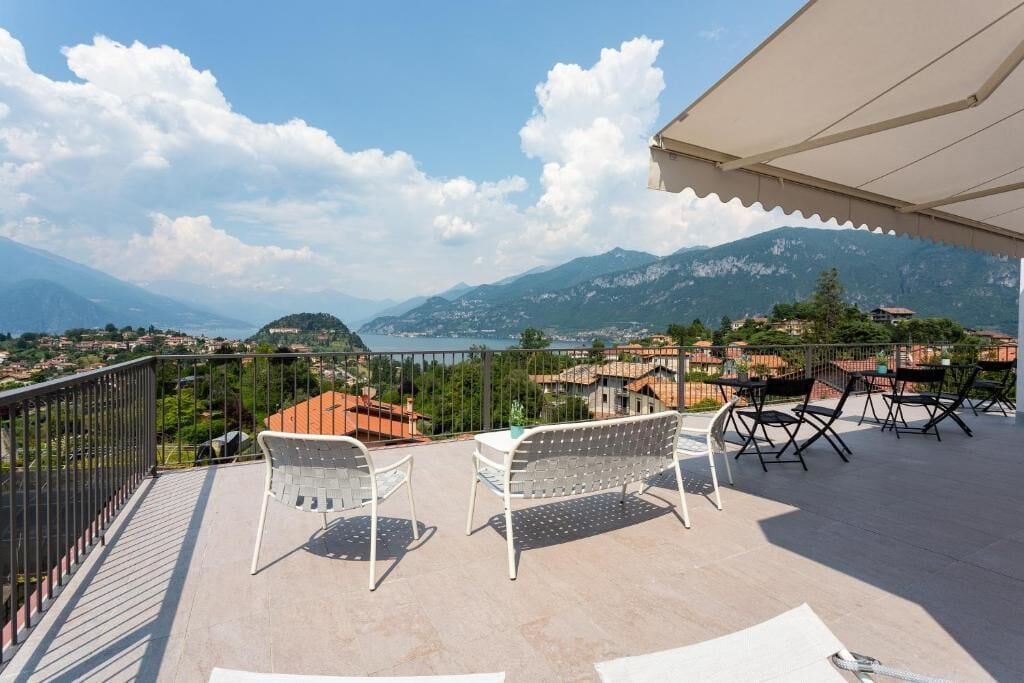 Ein Balkon mit Stühlen und Tisch, mit Blick auf eine Berglandschaft und ein Gewässer.