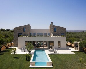 A modern two-story house with a swimming pool, outdoor seating, and a view of the countryside. - Citrus Grove Luxury Villas (Rethymno)