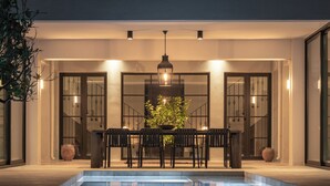 Ein Essbereich am Pool mit Tisch und Stühlen, einer hängenden Lampe und Kübelpflanzen.