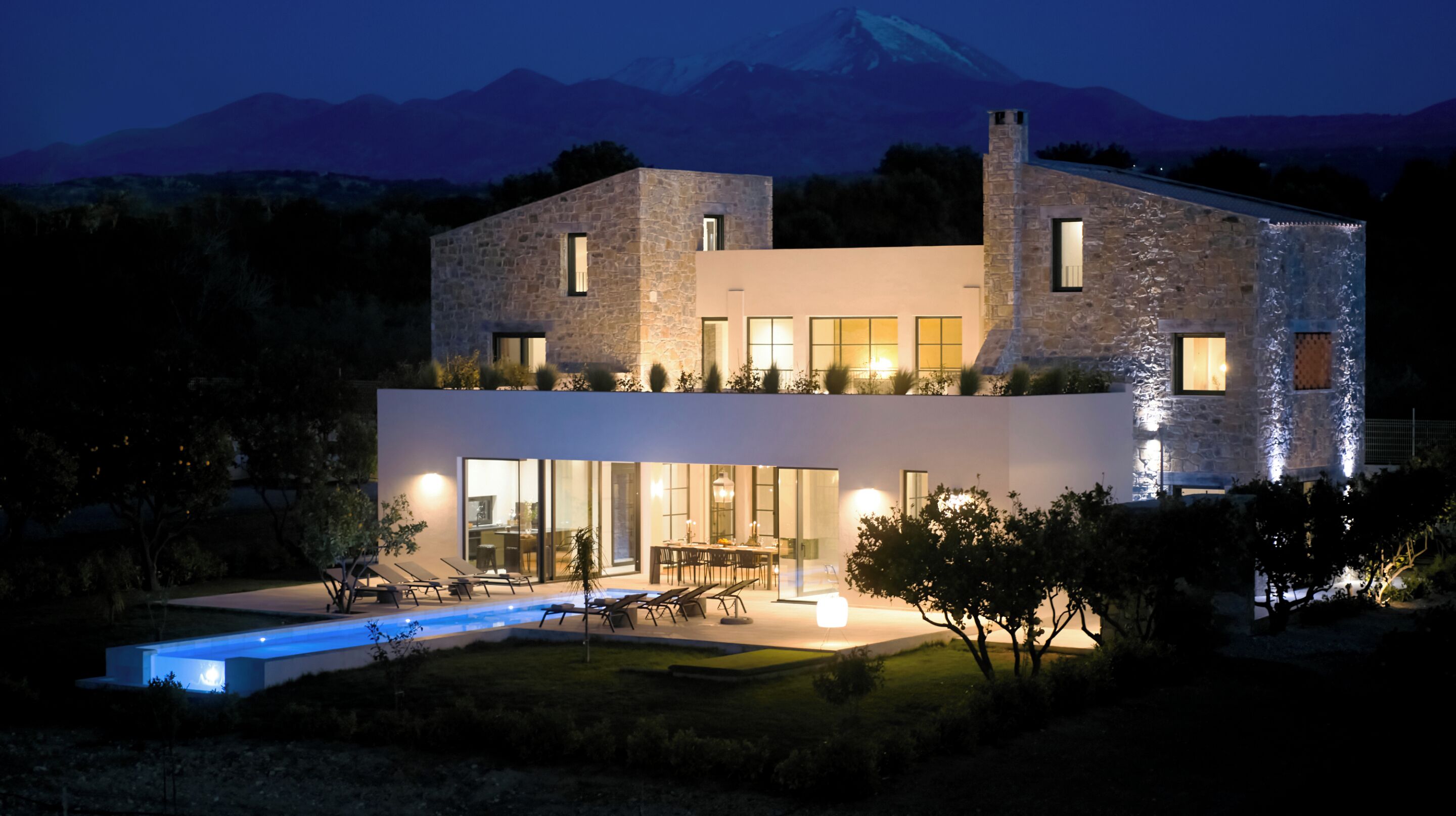 A modern two-story house with a swimming pool, large windows, and a mountain backdrop.