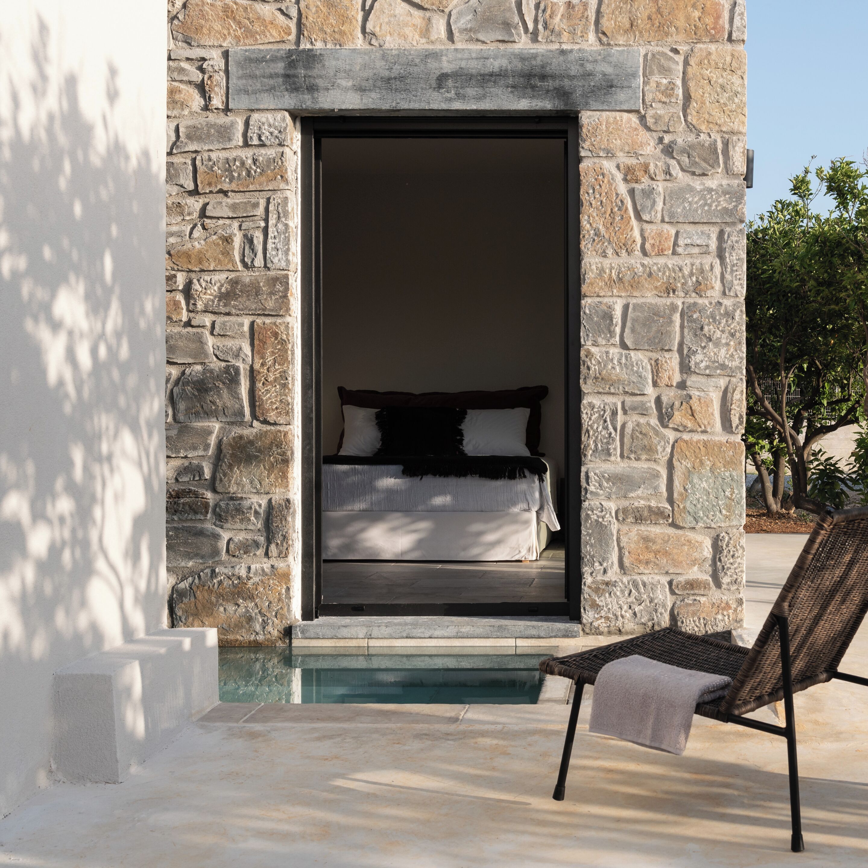 A stone exterior wall with a doorway leading to a bedroom with a bed and pillows.