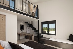 A modern bedroom with a large bed, a wooden desk, a staircase, and a view of the outdoors. - Citrus Grove Luxury Villas (Rethymno)